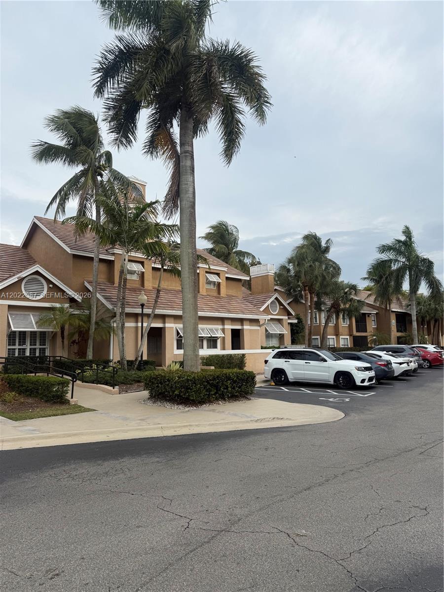A multi-story tan stucco apartment building features a tiled roof and several palm trees — 15689 SW 106th Ln # 718, Miami FL 33196, MIAMI, FL
