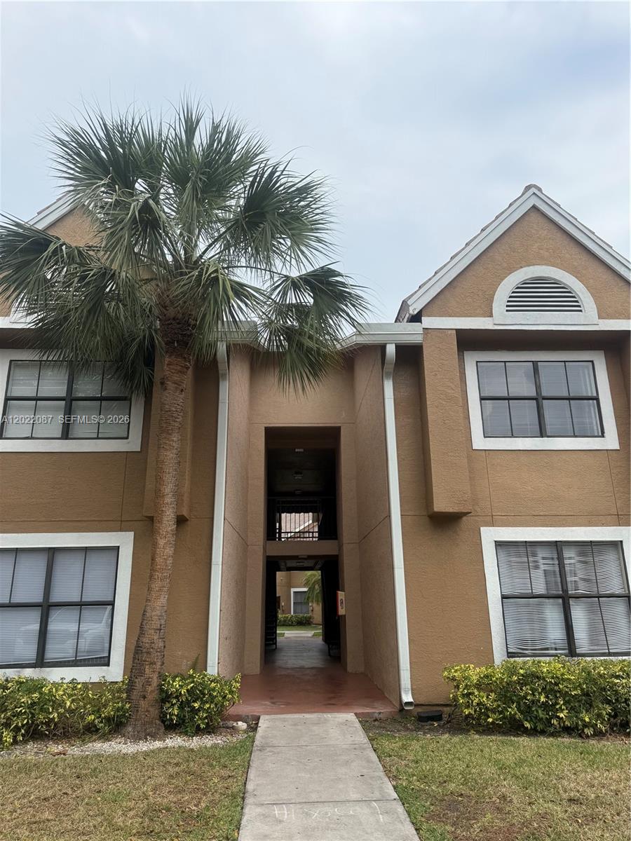 A two-story tan stucco apartment building features a central walkway and a prominent palm tree — 15689 SW 106th Ln # 718, Miami FL 33196, MIAMI, FL