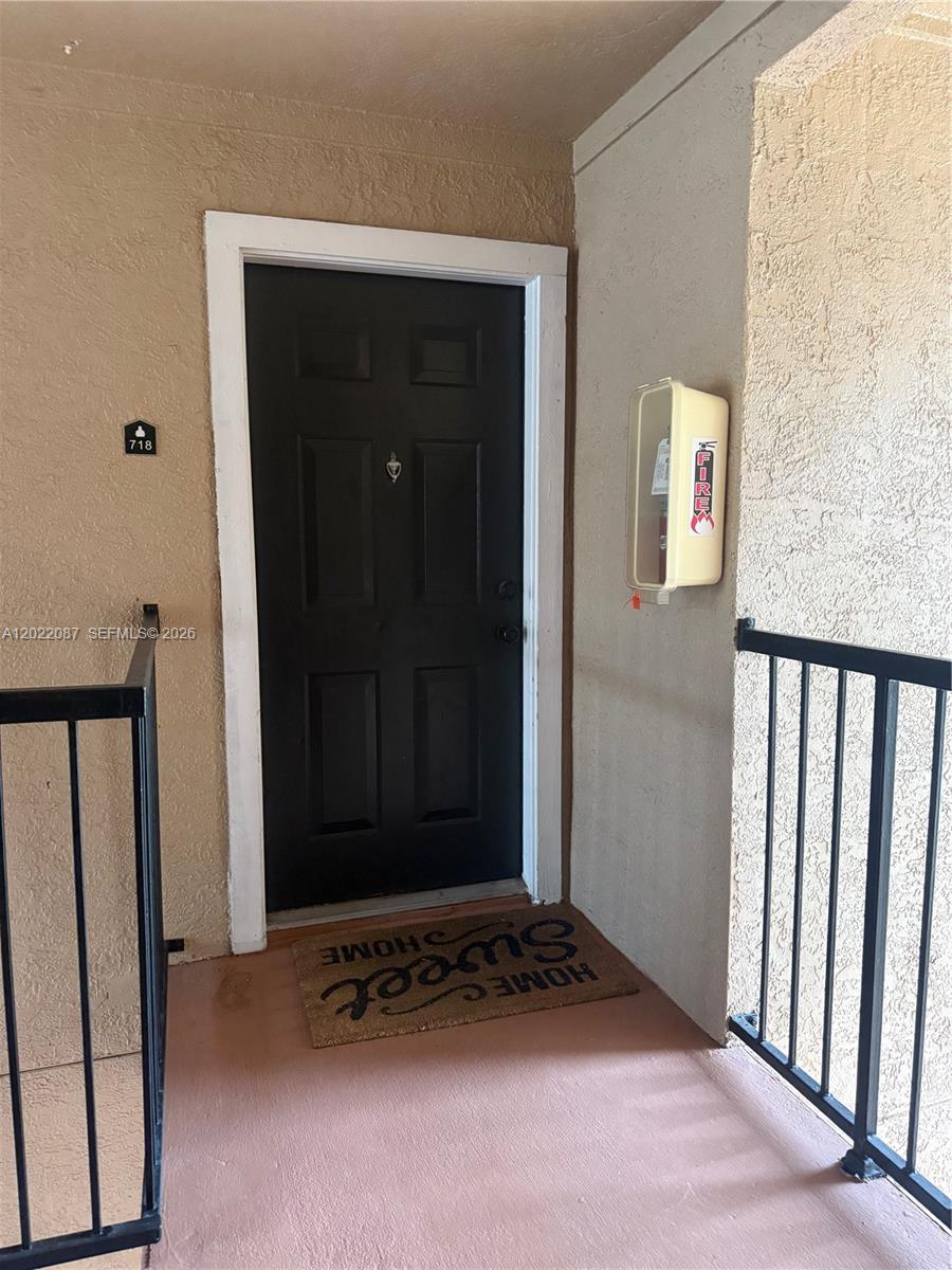 A black front door with a welcome mat and a fire extinguisher cabinet on the wall — 15689 SW 106th Ln # 718, Miami FL 33196, MIAMI, FL