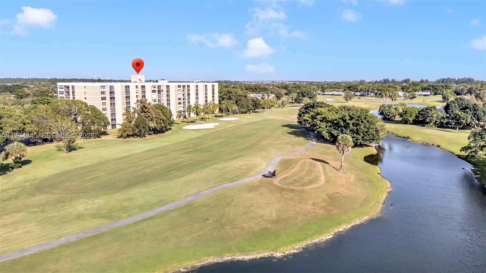 An aerial view shows a multi-story apartment building situated next to a golf course and lake — 16300 Golf Club Rd # 408, Weston FL 33326, WESTON, FL