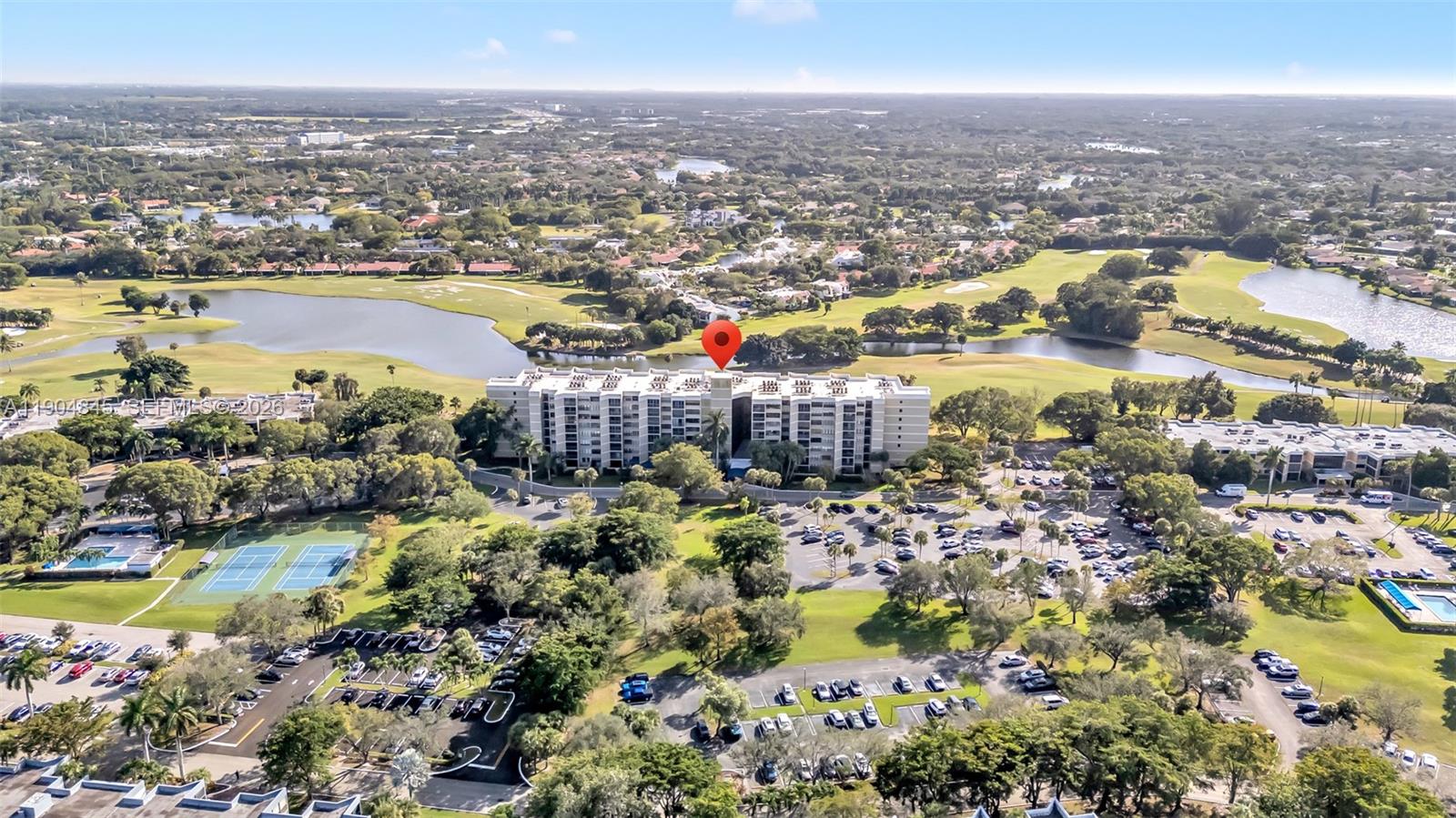 An aerial view shows a multi-story apartment building surrounded by a golf course and parking — 16300 Golf Club Rd # 408, Weston FL 33326, WESTON, FL