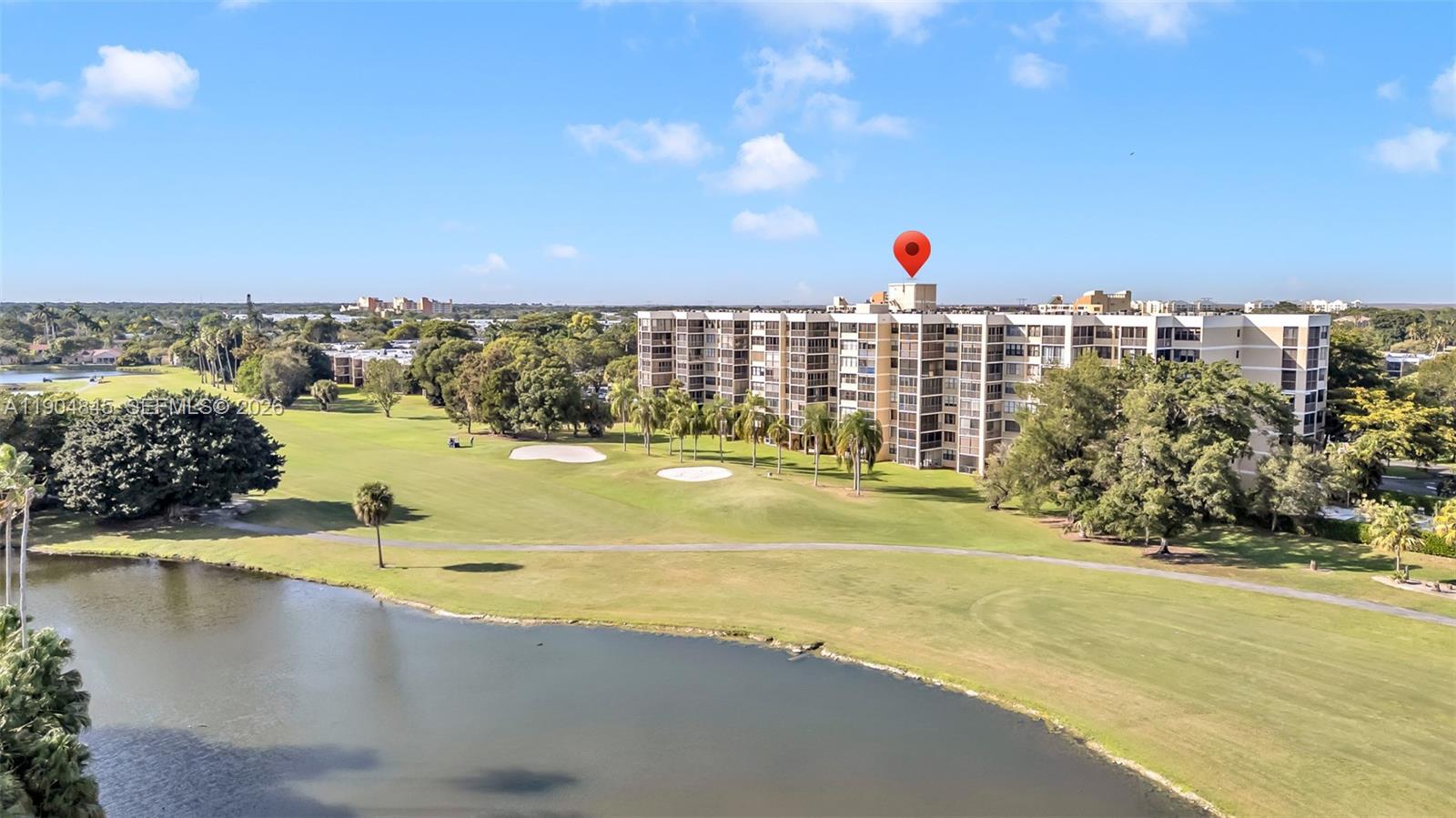 An aerial view shows a multi-story apartment building situated next to a golf course lake — 16300 Golf Club Rd # 408, Weston FL 33326, WESTON, FL