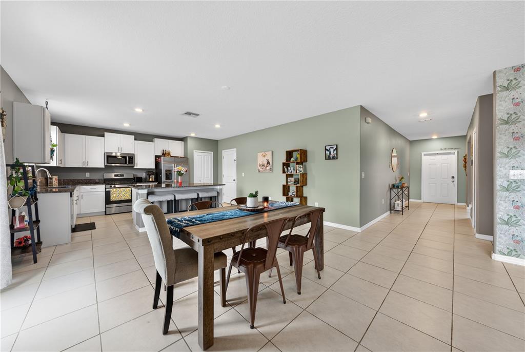 A dining area with a wooden table sits adjacent to an open-concept kitchen with white cabinets — 10291 SHADY PRESERVE DRIVE, RIVERVIEW, FL