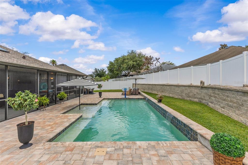 A backyard features a paved patio, a swimming pool, and a screened-in porch area — 14158 LEYBOURNE WAY, SPRING HILL, FL