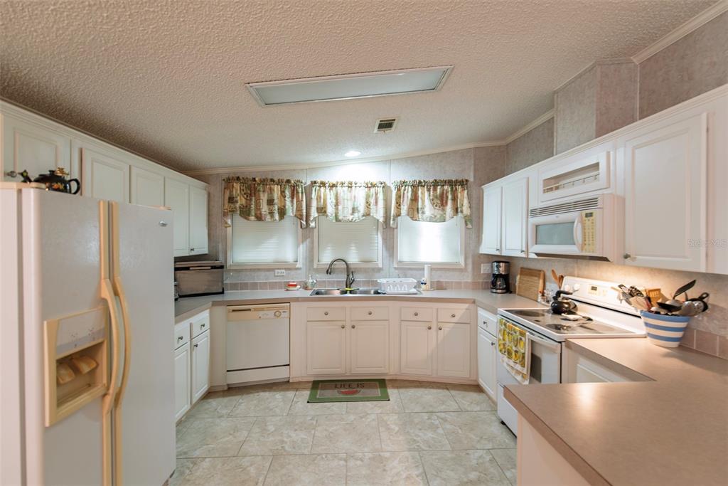 A kitchen with white cabinets, light countertops, tile flooring, and three windows above the sink — 3 ROTTERDAM DRIVE, PUNTA GORDA, FL