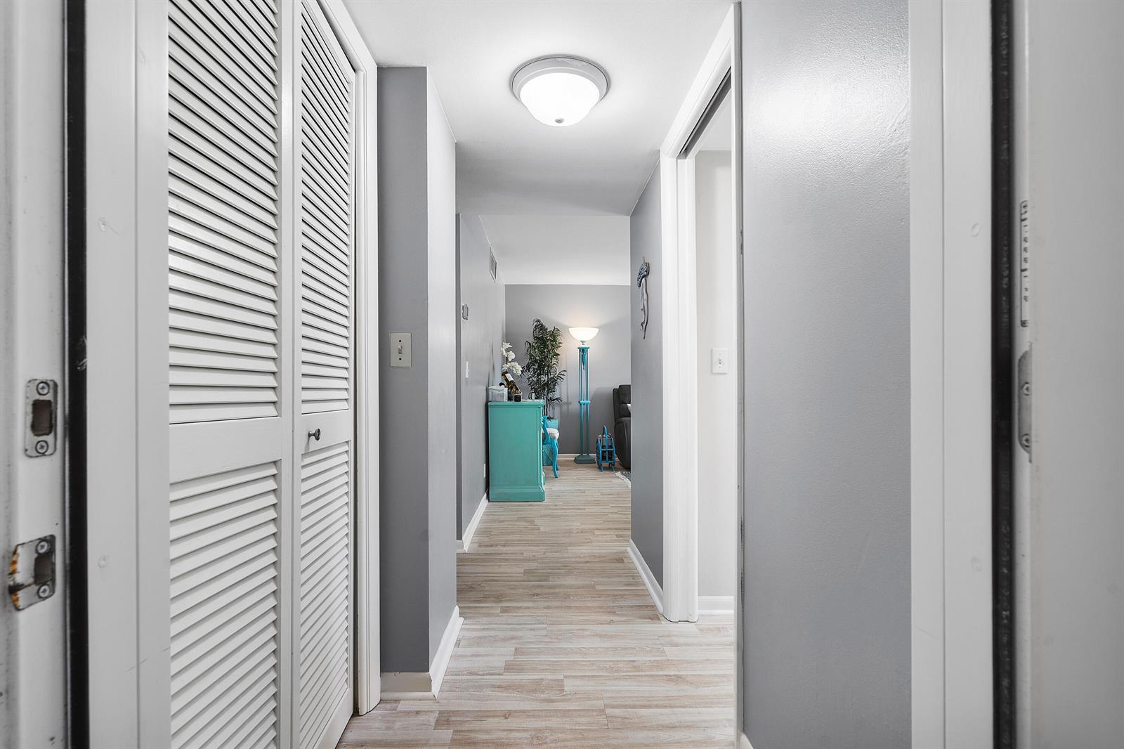 A hallway with light wood-look flooring, gray walls, and white louvered closet doors — 2525 Florida Boulevard # 130, Delray Beach FL 33483, DELRAY BEACH, FL