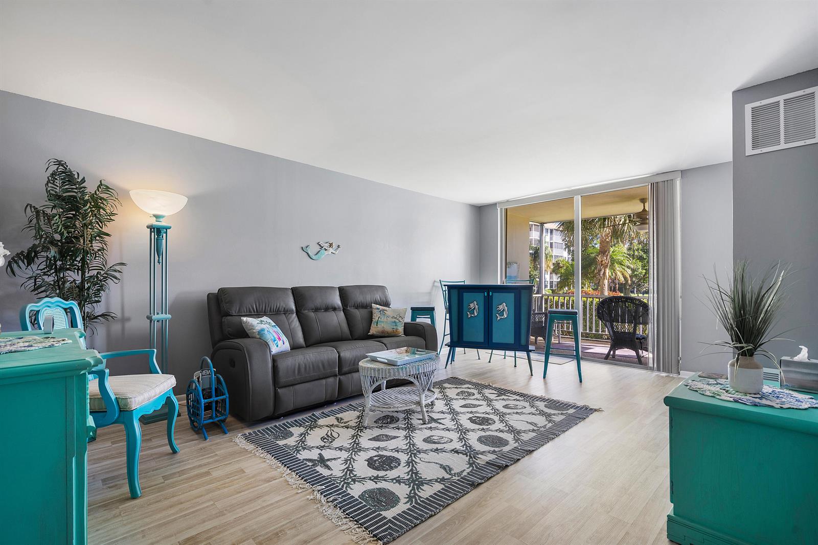 A living room features a gray sofa, a patterned rug, and bright teal furniture accents — 2525 Florida Boulevard # 130, Delray Beach FL 33483, DELRAY BEACH, FL
