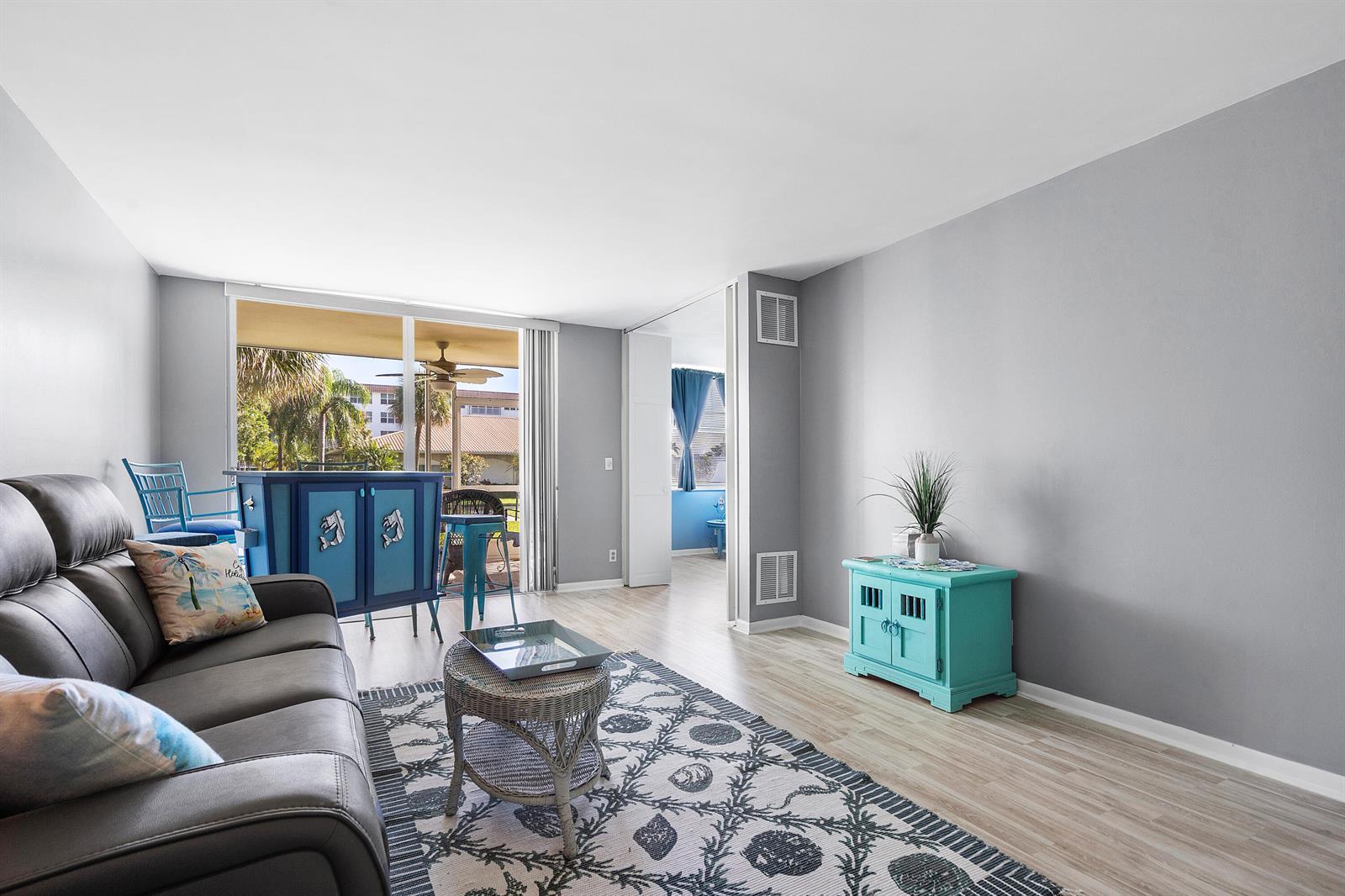 A living room features a gray sofa, a patterned rug, and a bright blue cabinet — 2525 Florida Boulevard # 130, Delray Beach FL 33483, DELRAY BEACH, FL