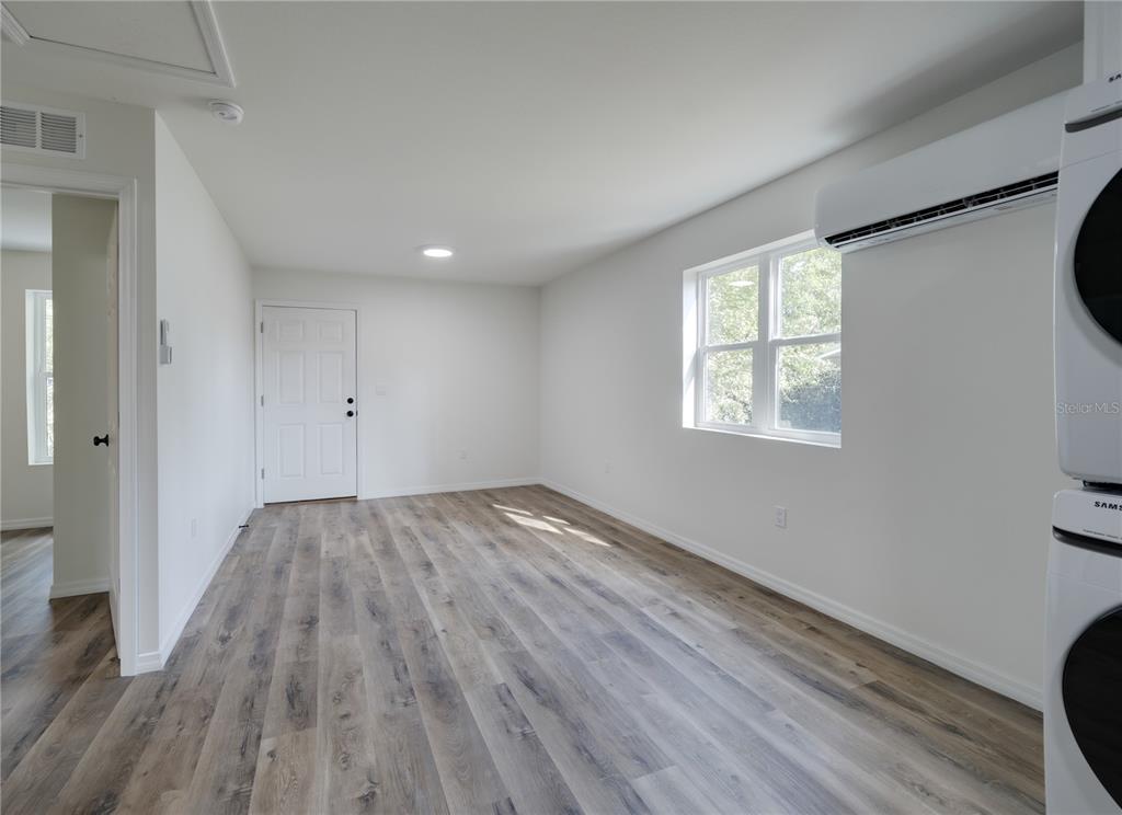 A bright room features light wood-look flooring, white walls, a window, and a stacked washer-dryer — 767 1/2 19TH AVENUE S, ST PETERSBURG, FL