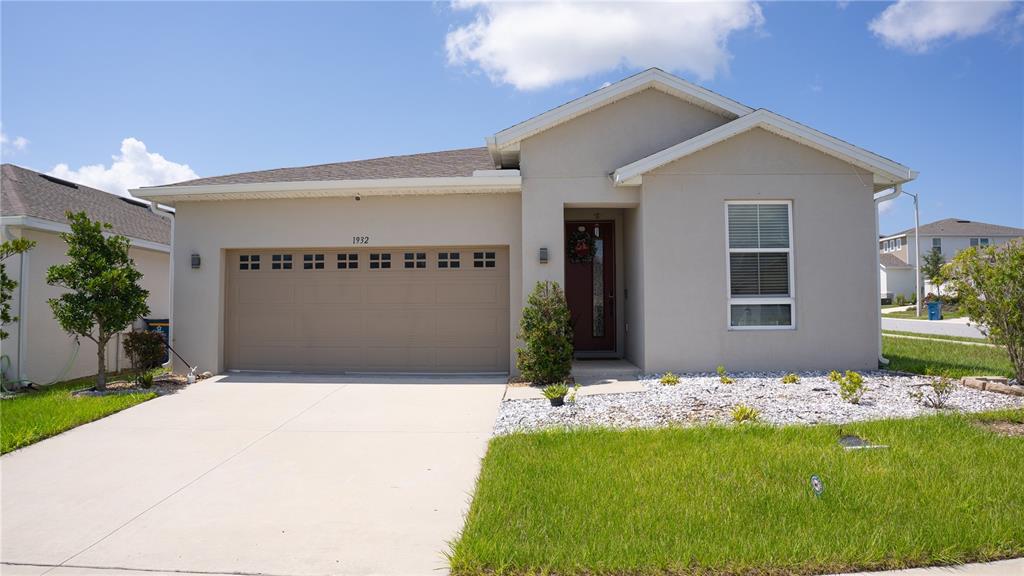 A single-story house with a beige stucco exterior, a two-car garage, and a front lawn — 1932 CHICKASAW BOULEVARD, DAVENPORT, FL