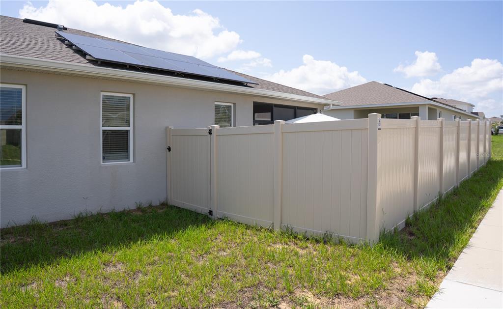A beige vinyl fence encloses the backyard of a house with solar panels on the roof — 1932 CHICKASAW BOULEVARD, DAVENPORT, FL