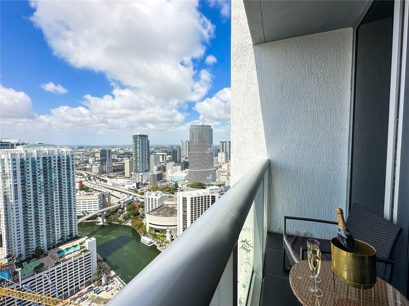 A balcony view overlooks a city skyline with a river and a table with champagne — 485 Brickell Ave # 4405, Miami FL 33131, MIAMI, FL