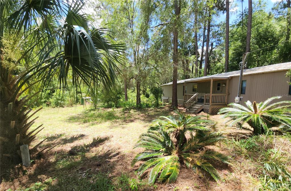 A mobile home with a wooden porch sits in a yard surrounded by trees — 22835 SW 117TH PLACE ROAD, DUNNELLON, FL