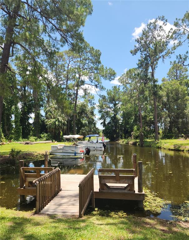 A wooden dock with built-in benches sits on a canal with two pontoon boats moored — 22835 SW 117TH PLACE ROAD, DUNNELLON, FL