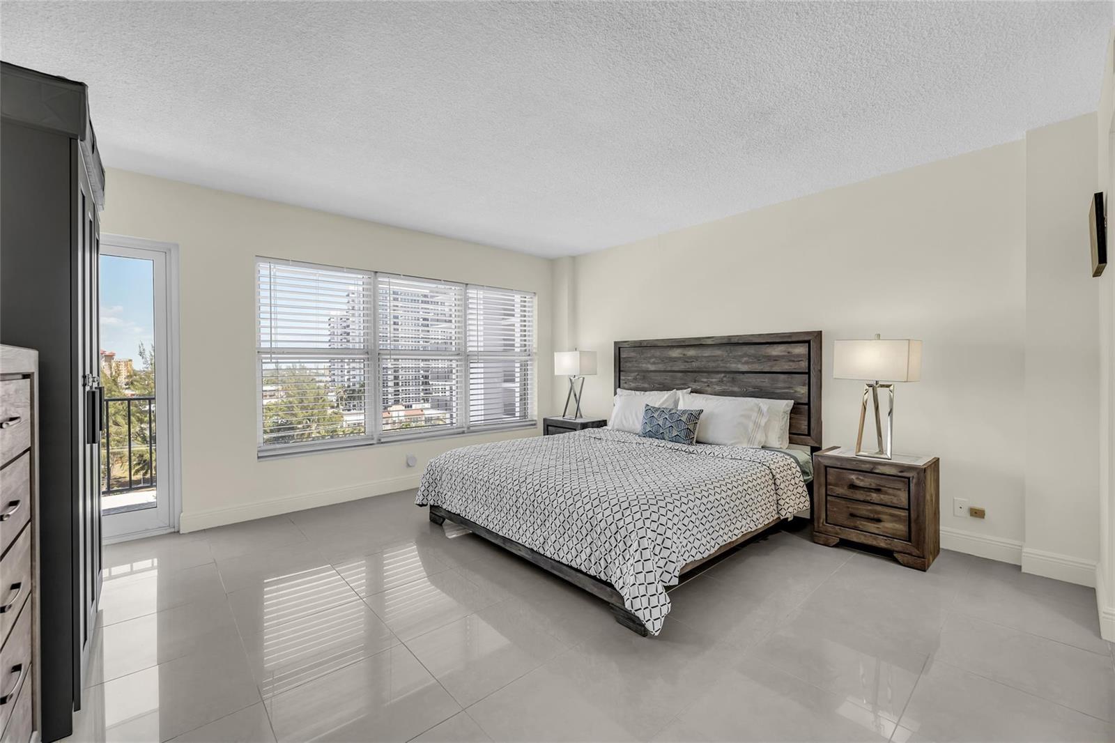 A bedroom with tile floors, a wooden bed frame, and a balcony door — 405 N Ocean Boulevard # 727, Pompano Beach FL 33062, POMPANO BEACH, FL