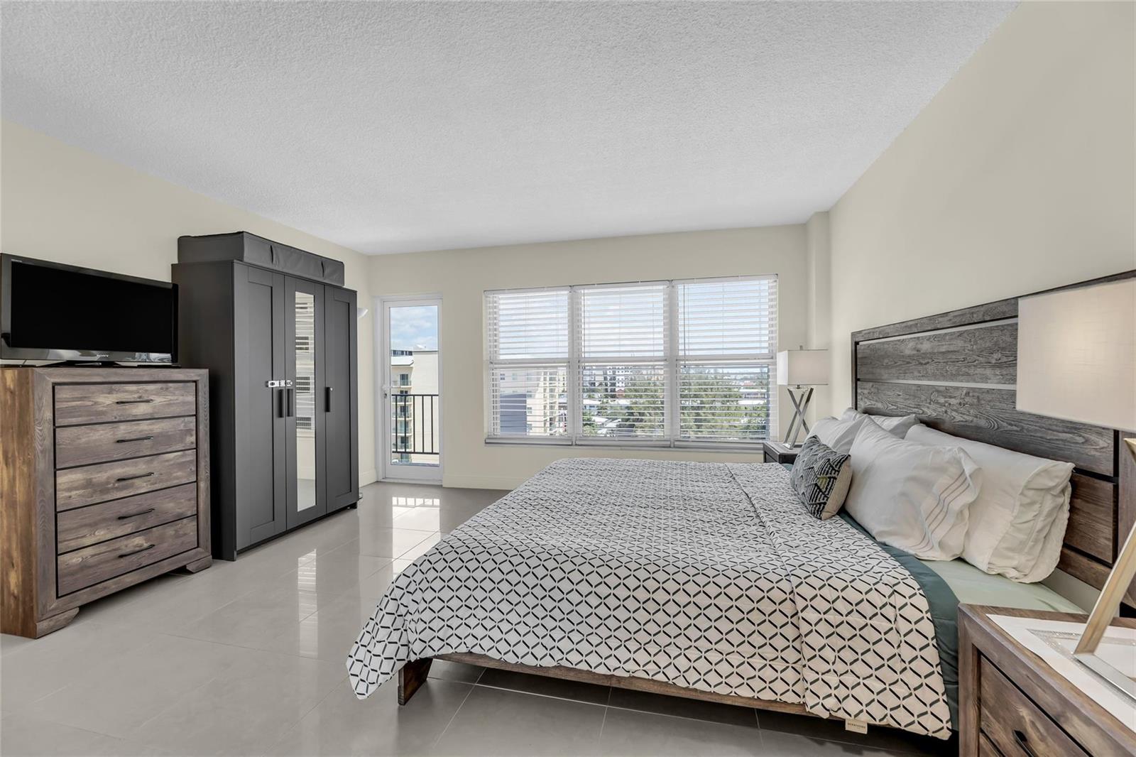 A bedroom with tile floors, a wooden bed frame, a wardrobe, and a balcony door — 405 N Ocean Boulevard # 727, Pompano Beach FL 33062, POMPANO BEACH, FL