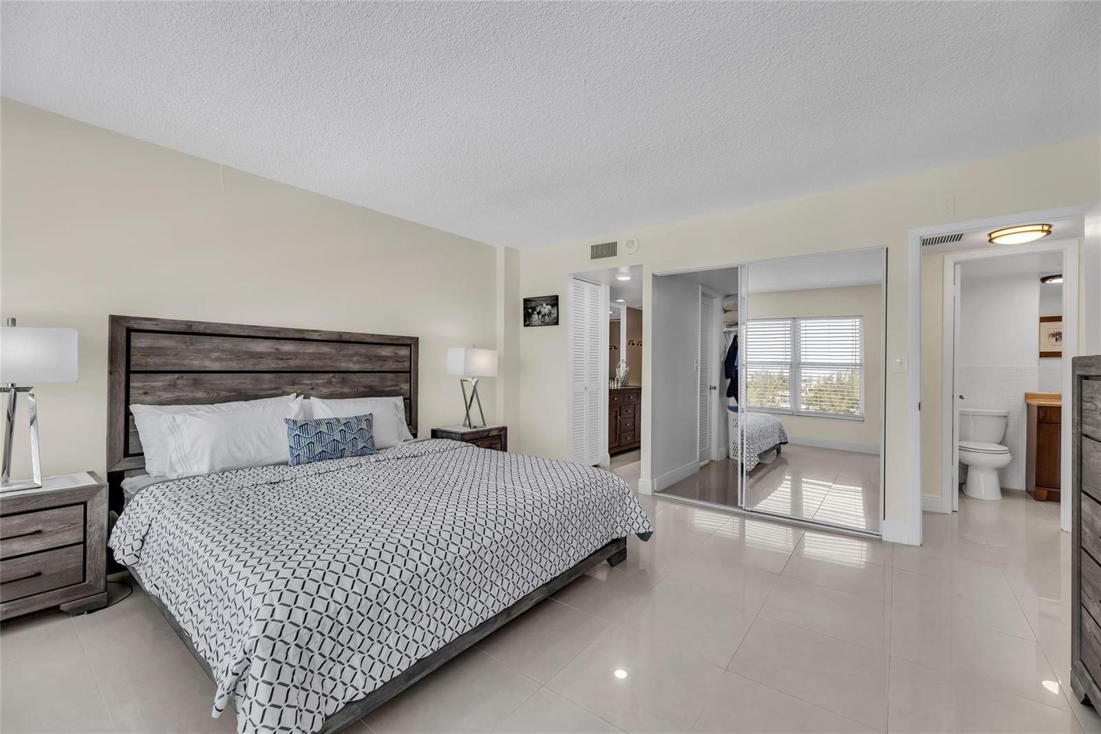 A bedroom with a king bed, mirrored closet doors, and light-colored tile flooring — 405 N Ocean Boulevard # 727, Pompano Beach FL 33062, POMPANO BEACH, FL