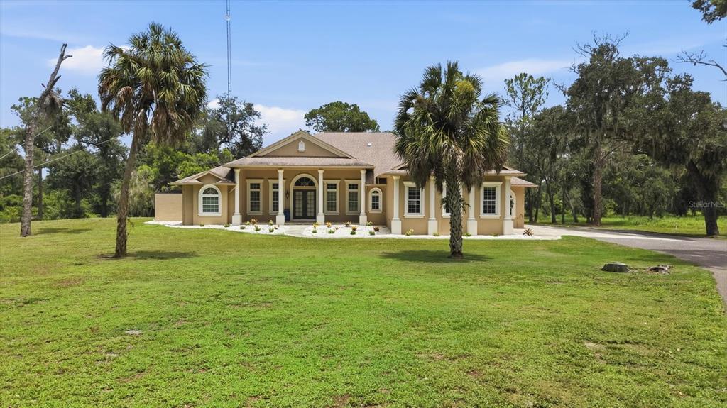 A tan, single-story house with white columns and palm trees sits on a grassy lot — 24525 JENNINGS ROAD, MYAKKA CITY, FL