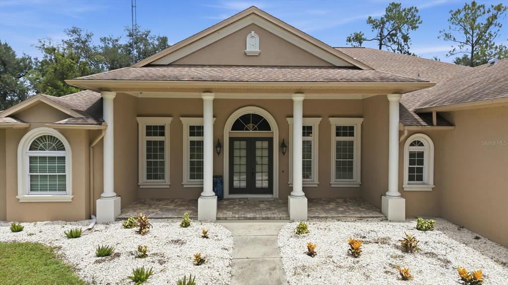 The exterior of a tan house features a covered porch with white columns and windows — 24525 JENNINGS ROAD, MYAKKA CITY, FL