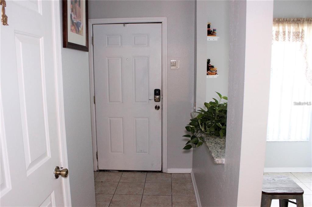 An entryway features a white front door, tile flooring, and a small granite-topped ledge — 1247 REDONDO WAY UNIT 1247, WESLEY CHAPEL, FL