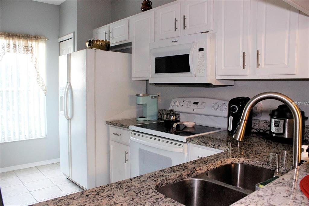 A kitchen features white cabinets, granite countertops, a double sink, and white appliances — 1247 REDONDO WAY UNIT 1247, WESLEY CHAPEL, FL