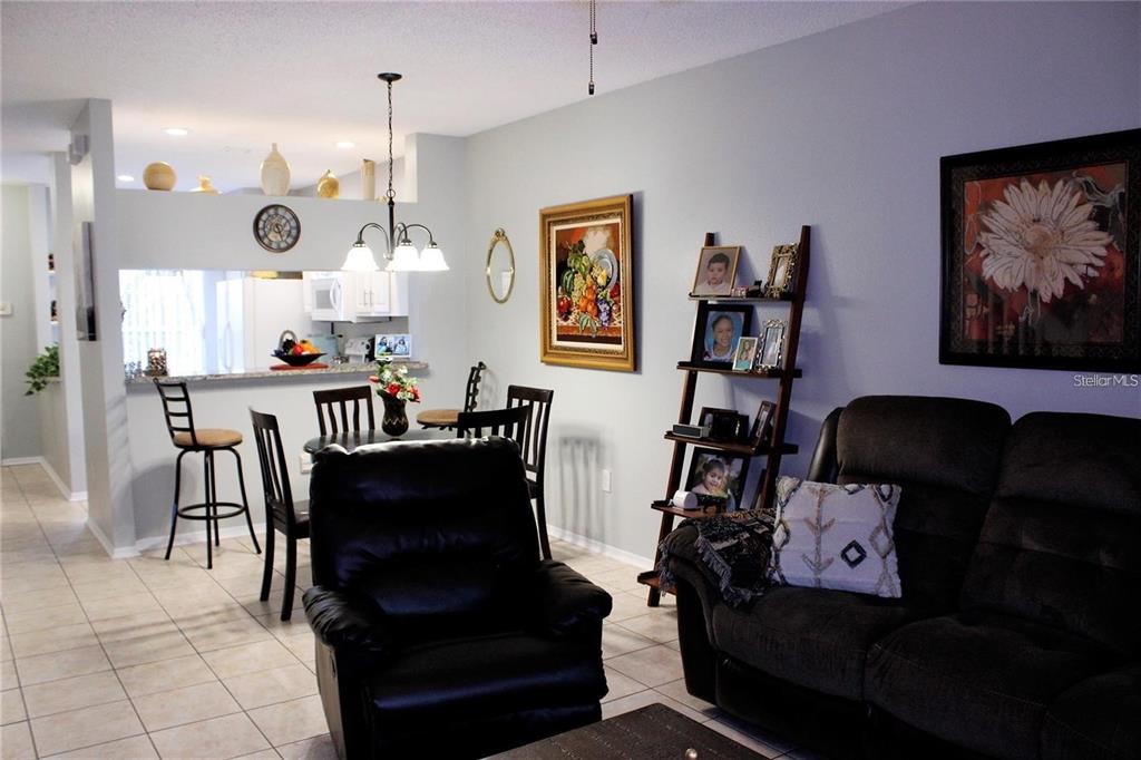 A living room with a recliner and sofa opens to a dining area and kitchen — 1247 REDONDO WAY UNIT 1247, WESLEY CHAPEL, FL