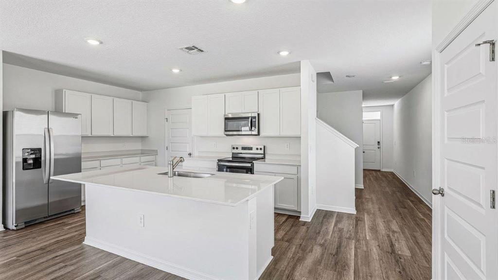 A modern kitchen features white cabinetry, stainless steel appliances, a center island, and wood-look flooring — 6064 NAVONA WAY, WINTER HAVEN, FL
