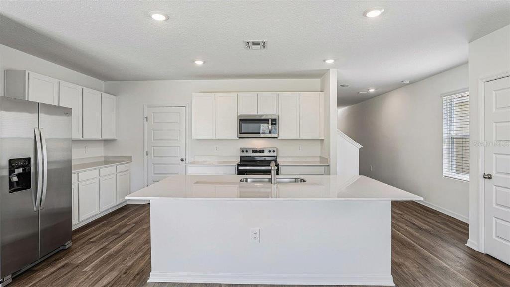 A modern kitchen features white cabinetry, stainless steel appliances, and a large central island — 6064 NAVONA WAY, WINTER HAVEN, FL