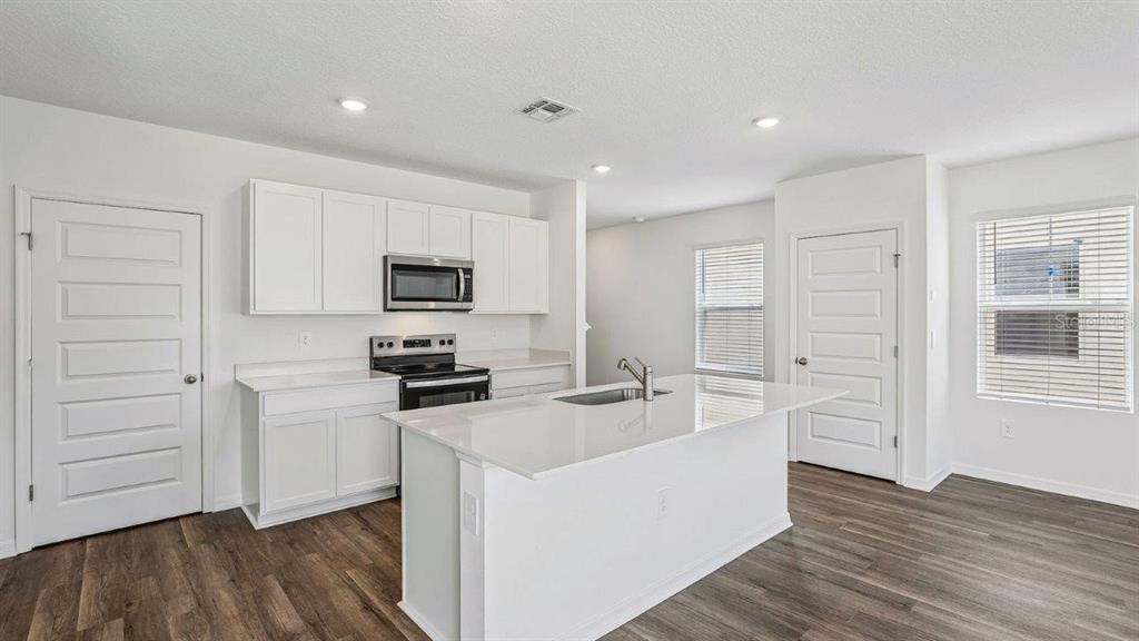 A modern kitchen features white cabinets, stainless steel appliances, a center island, and wood-look flooring — 6064 NAVONA WAY, WINTER HAVEN, FL