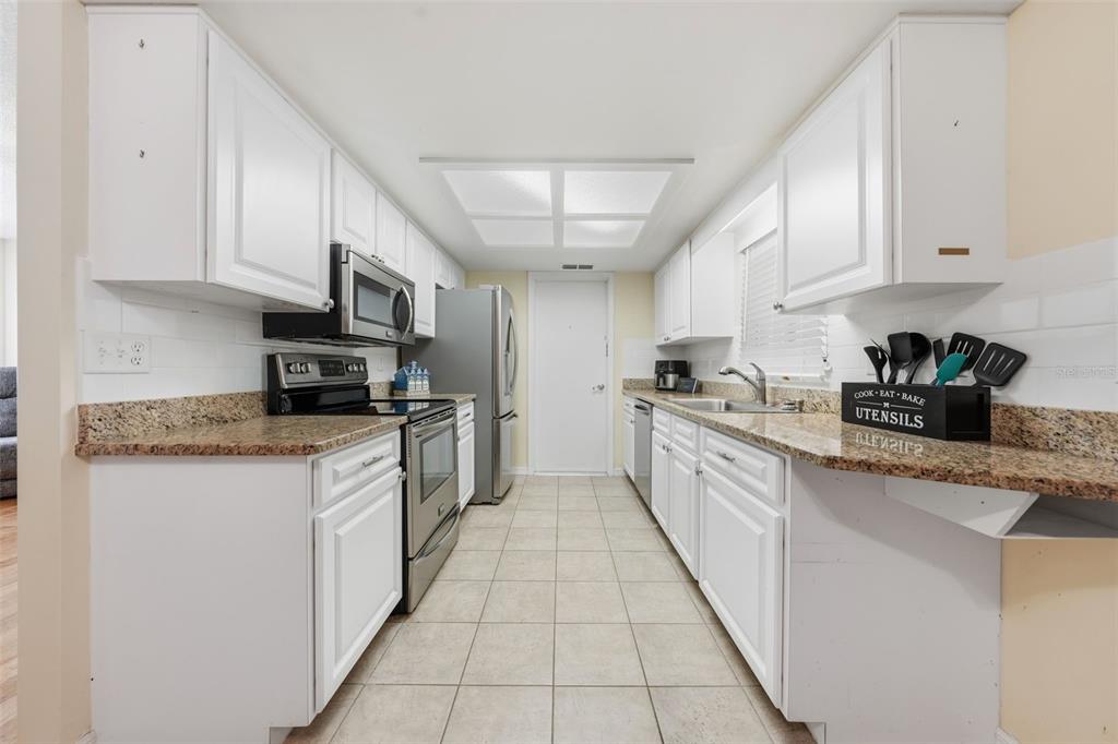 A galley kitchen features white cabinets, granite countertops, stainless steel appliances, and tile flooring — 11224 SW 79TH TERRACE, OCALA, FL