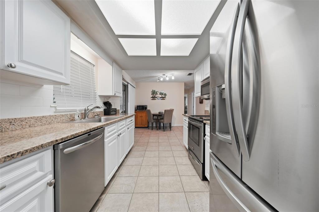A kitchen with white cabinets, granite countertops, stainless steel appliances, and tile flooring — 11224 SW 79TH TERRACE, OCALA, FL