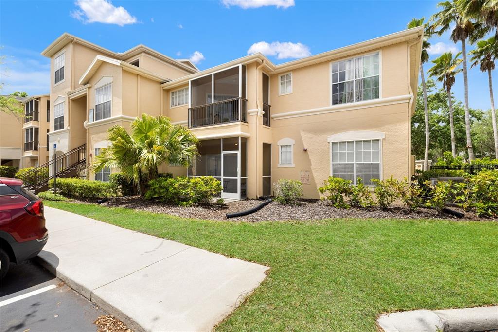 A two-story tan apartment building with screened-in balconies and a landscaped lawn — 5125 PALM SPRINGS BOULEVARD UNIT 13104, TAMPA, FL