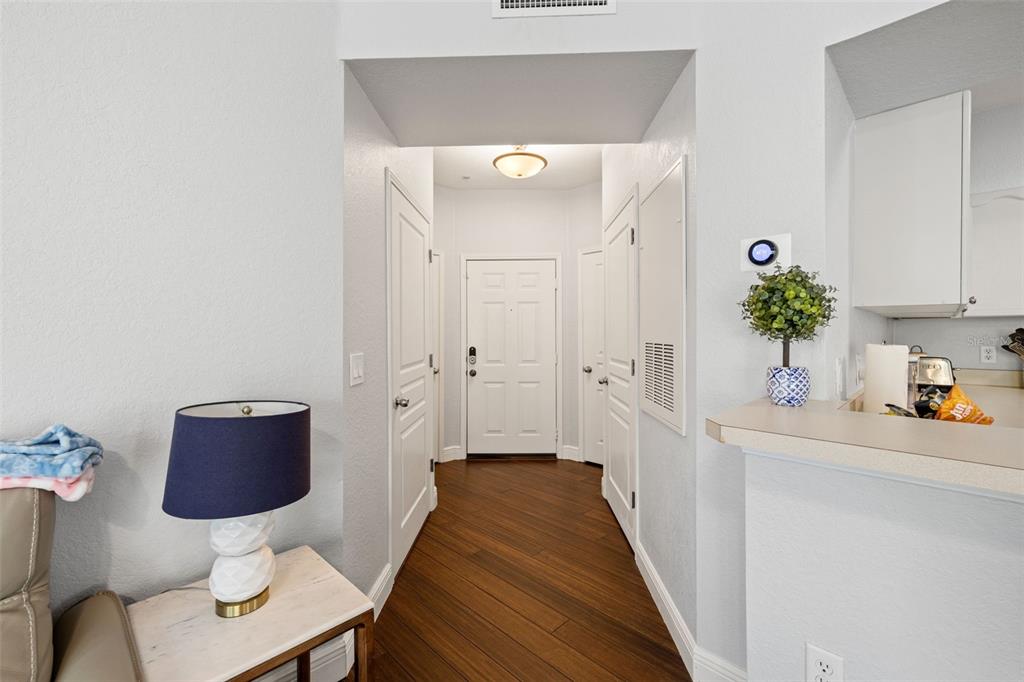 A hallway with wood flooring leads to a white front door near a kitchen counter — 5125 PALM SPRINGS BOULEVARD UNIT 13104, TAMPA, FL