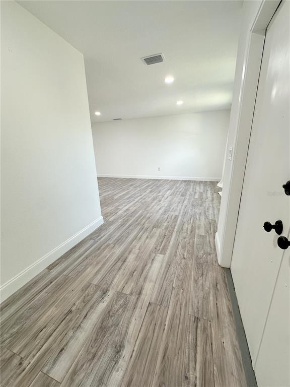 A hallway with light wood-look flooring leads into a large, empty room with white walls — 1081 HUMBOLDT STREET, ENGLEWOOD, FL