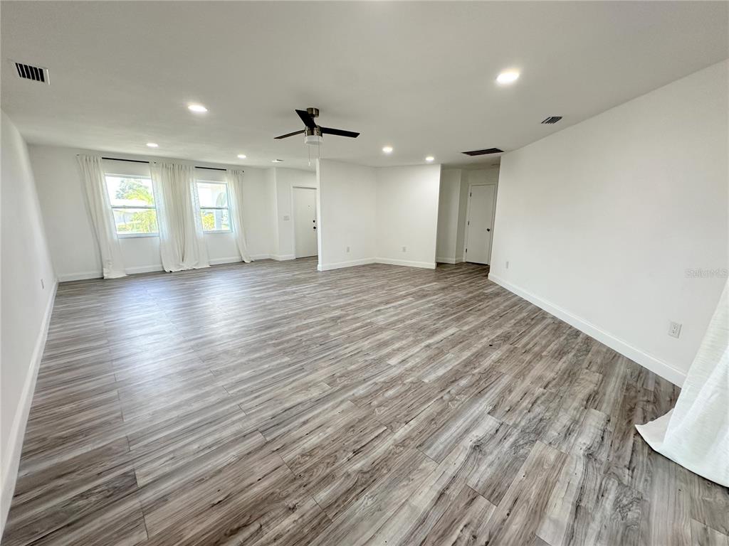 A spacious, empty room features light wood-look flooring, white walls, and a ceiling fan — 1081 HUMBOLDT STREET, ENGLEWOOD, FL