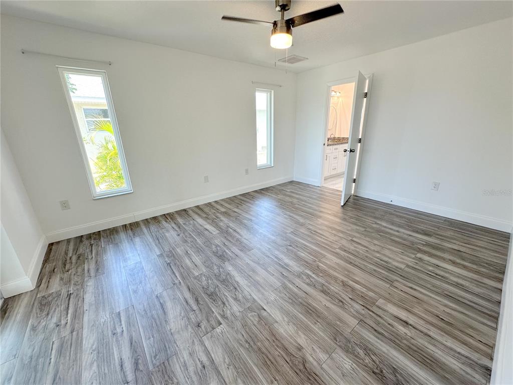A bedroom with white walls, wood-look flooring, a ceiling fan, and an attached bathroom — 1081 HUMBOLDT STREET, ENGLEWOOD, FL