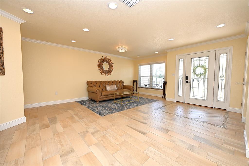 A living room with light wood-look tile flooring, a tan tufted sofa, and a front door — 2240 LAKE ARIANA BOULEVARD, AUBURNDALE, FL