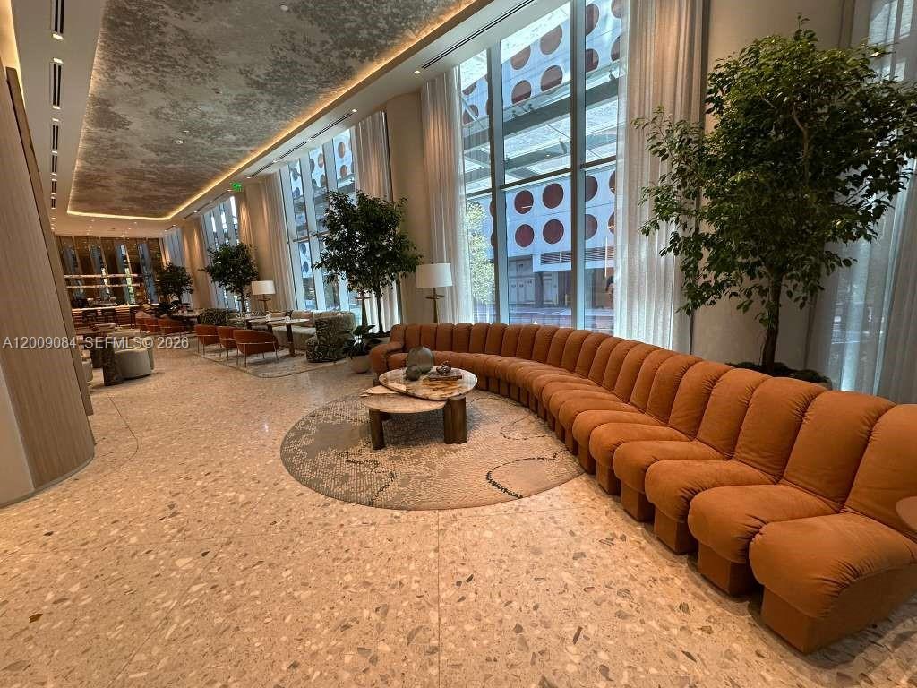 A spacious lobby features a long, curved orange sofa, potted trees, and large floor-to-ceiling windows — 77 SE 5th Street # 3115, Miami FL 33131, MIAMI, FL