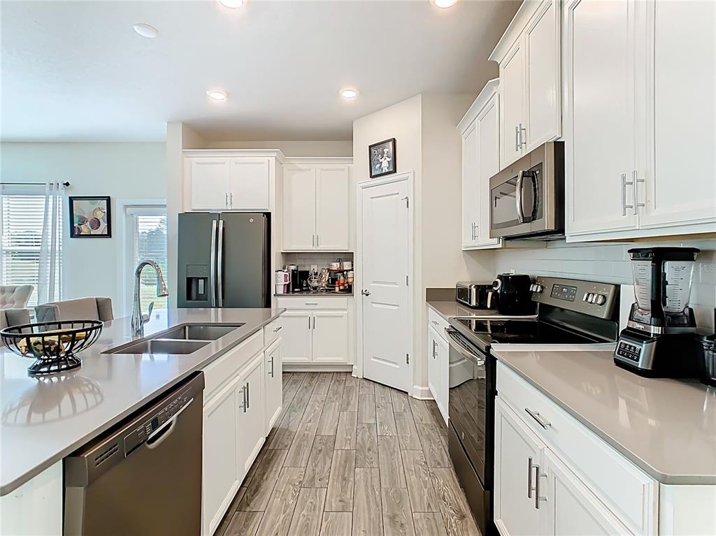 A modern kitchen features white cabinets, stainless steel appliances, gray countertops, and wood-look tile flooring — 1059 BLACKWOLF RUN ROAD, DAVENPORT, FL