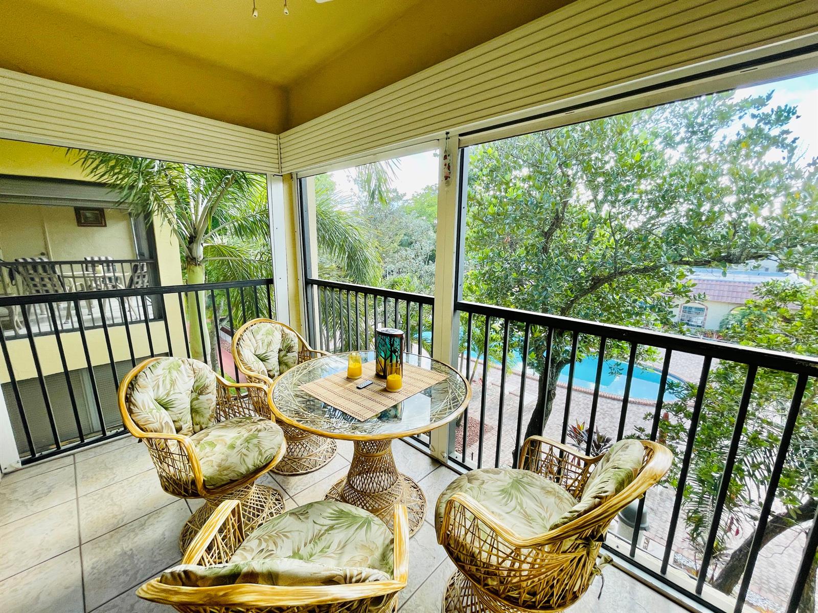 A screened-in balcony features a wicker table and chairs overlooking a swimming pool — 257 S Cypress Road # 442, Pompano Beach FL 33060, POMPANO BEACH, FL