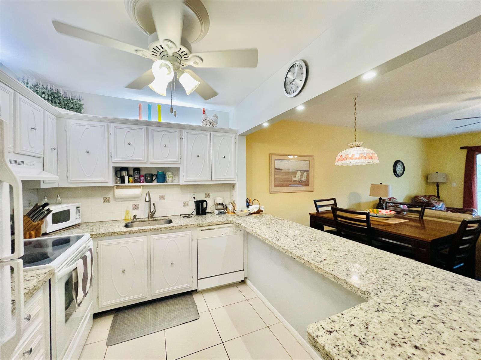 A kitchen with white cabinets, granite countertops, and a breakfast bar overlooking a dining area — 257 S Cypress Road # 442, Pompano Beach FL 33060, POMPANO BEACH, FL