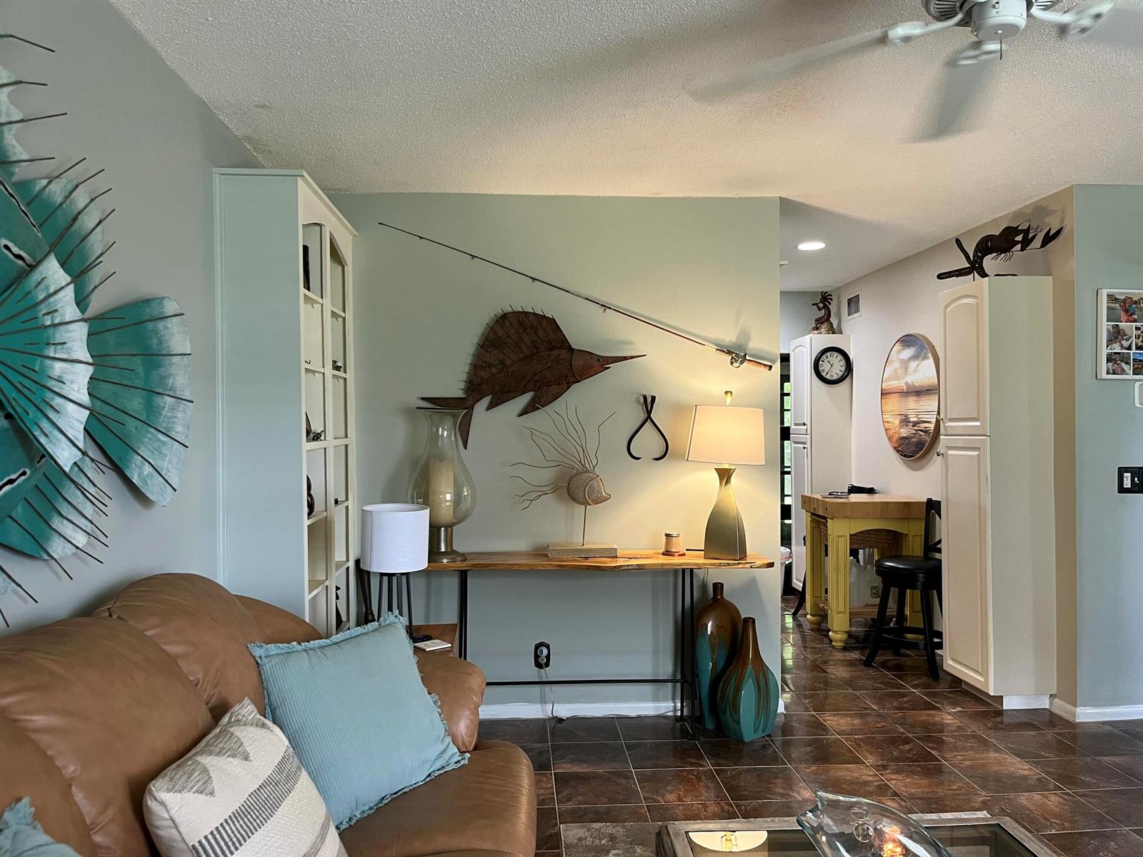 A living room features a brown leather sofa with decorative pillows and metal fish art — 915 Riverwood Lane, Jupiter FL 33458, JUPITER, FL