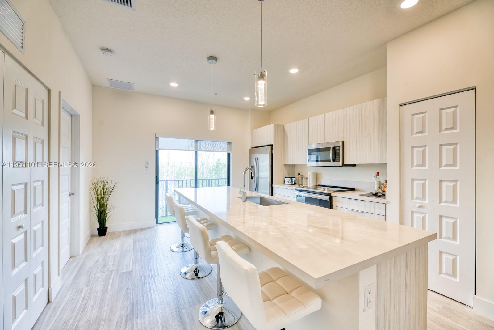 A modern kitchen features a large quartz island, white cabinetry, and stainless steel appliances — 7831 NW 104th Ave # 23, Doral FL 33178, DORAL, FL