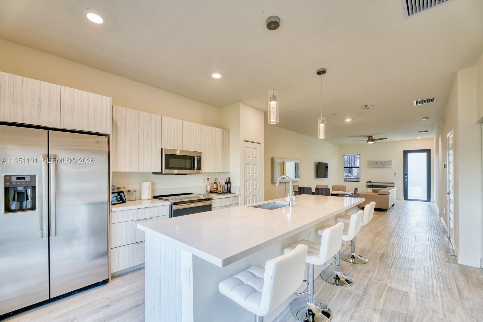 A modern kitchen features light wood cabinetry, white countertops, a large island, and stainless appliances — 7831 NW 104th Ave # 23, Doral FL 33178, DORAL, FL