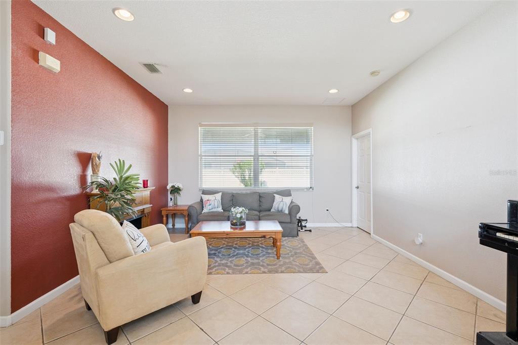 A living room features a red accent wall, tile flooring, and a gray sofa — 2930 WHITE CEDAR CIRCLE, KISSIMMEE, FL