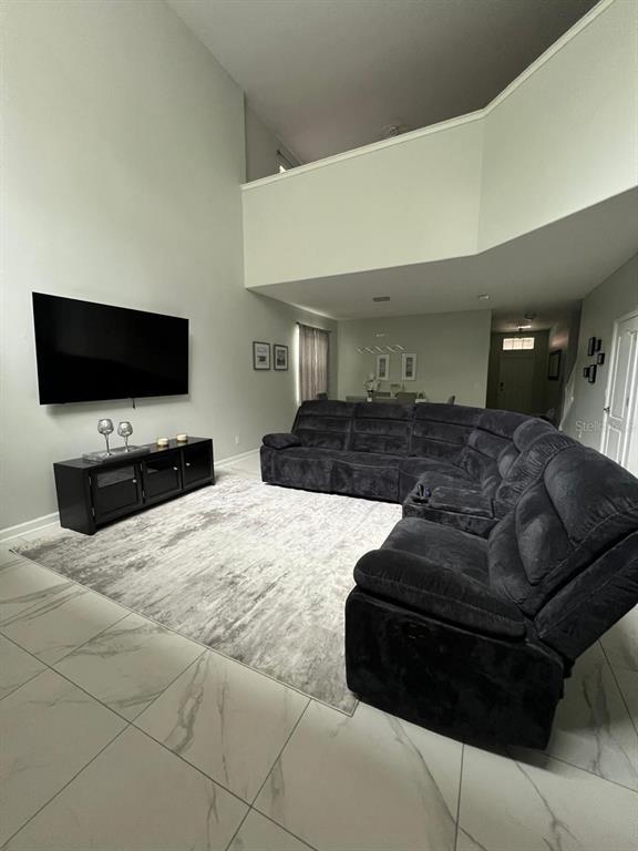 A living room features a large sectional sofa, a wall-mounted television, and tiled flooring — 8894 CANDY PALM ROAD, KISSIMMEE, FL