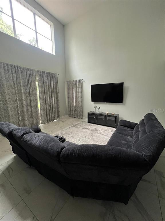 A living room features a large sectional sofa, a wall-mounted television, and floor-to-ceiling windows — 8894 CANDY PALM ROAD, KISSIMMEE, FL