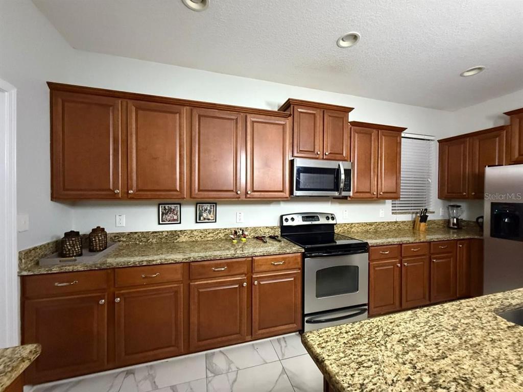 A kitchen features wood cabinets, granite countertops, stainless steel appliances, and white tiled flooring — 8894 CANDY PALM ROAD, KISSIMMEE, FL