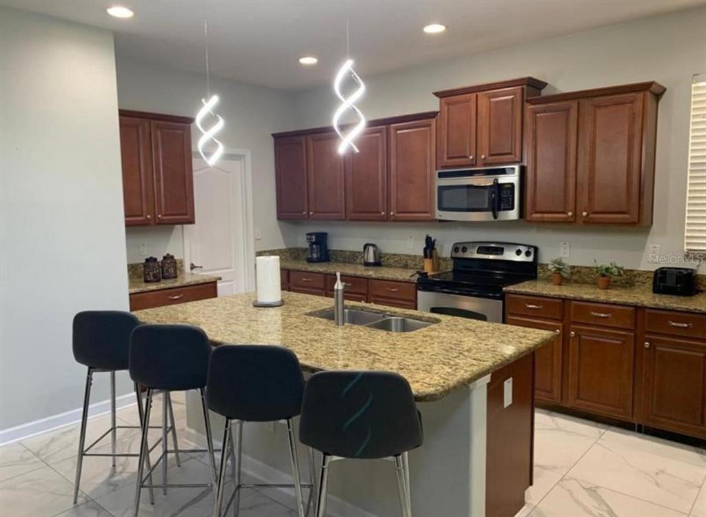 A kitchen features a granite island with four bar stools, wood cabinets, and stainless appliances — 8894 CANDY PALM ROAD, KISSIMMEE, FL