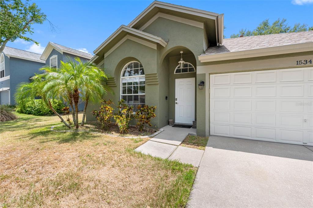 A single-story house with a green stucco exterior, a white garage door, and a palm tree — 1534 SCOTCH PINE DRIVE, BRANDON, FL